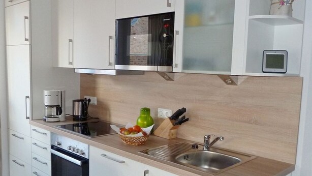Une cuisine moderne avec des meubles blancs, un four encastré, une machine à café et un évier.