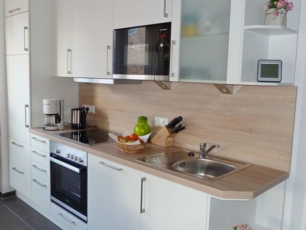 Una cocina moderna con armarios blancos, horno integrado, cafetera y lavabo.
