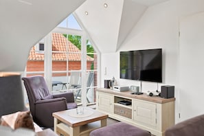 A modern living room with a TV, speakers, and a dining area. - Amelie - Wonderful vacation apartment in the village center (Krummhörn)