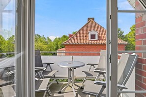 Ein Balkon mit Tisch und Stühlen, ein rotes Backsteingebäude im Hintergrund und ein klarer Himmel.