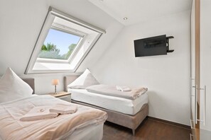 A bedroom with a skylight, two beds, a bedside table with a lamp, and a mounted TV. - Amelie - Wonderful vacation apartment in the village center (Krummhörn)