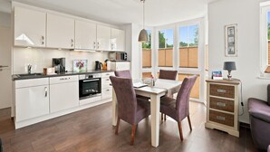 A modern kitchen with white cabinets, a dining table with chairs, and a view of the outdoors through large windows.