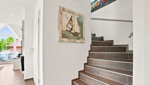 A staircase with wooden steps leading to a landing, a framed painting on the wall, and a view of an outdoor area with a pool.