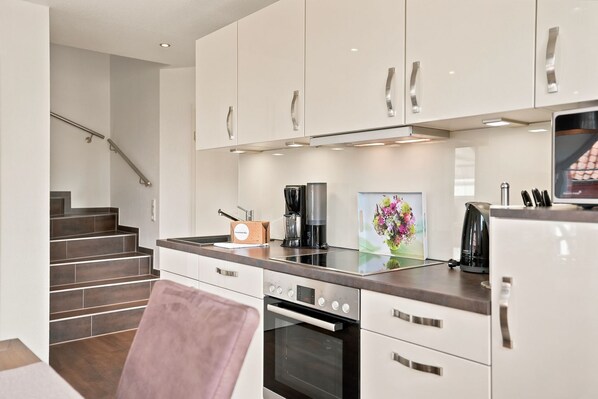 A modern kitchen with white cabinets, a stainless steel range hood, a coffee maker, and a vase with flowers on the counter.