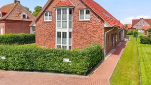A red brick house with a gabled roof, a central chimney, and a well-maintained lawn.