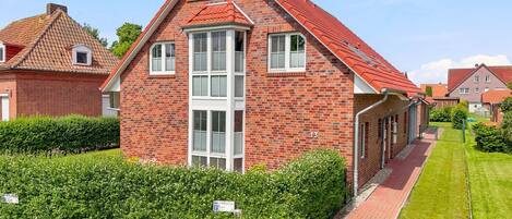 Une maison en briques rouges, avec un toit à pignon, une cheminée centrale et une pelouse bien entretenue.