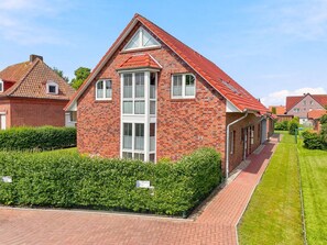 A red brick house with a gabled roof, a central chimney, and a well-maintained lawn.