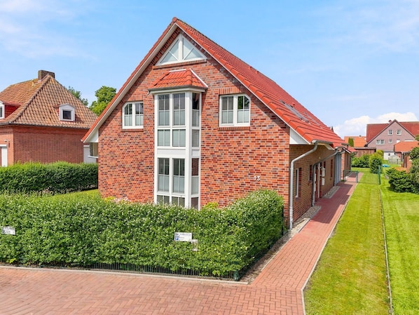 A red brick house with a gabled roof, a central chimney, and a well-maintained lawn. - Amelie - Wonderful vacation apartment in the village center (Krummhörn)