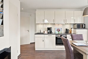 A modern kitchen with white cabinets, a microwave, a coffee maker, and a dining area with a table and chairs.