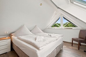 A bedroom with a bed, a nightstand, a chair, a window, and a skylight.