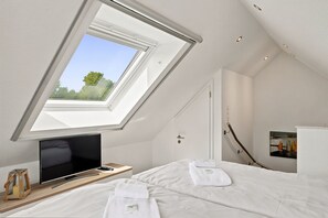 A bedroom with a skylight, a bed, a bedside table with a TV, and a painting on the wall. - Amelie - Wonderful vacation apartment in the center of the village (Krummhörn)