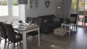 Un salon chaleureux avec un canapé, une table à manger dressée pour quatre personnes et une petite table d’appoint.