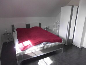 A modern bedroom with a bed, a wardrobe, and a small table with a lamp.