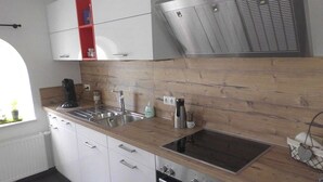 A modern kitchen with white cabinets, a wooden countertop, stainless steel appliances, and a window providing natural light. - Riedhaus am Siel - 100sqm vacation home for 6 pers. + dog with fireplace, heat cabin & (Krummhörn)