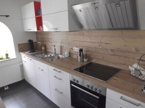 Una cocina moderna con armarios blancos, encimera de madera y electrodomésticos de acero inoxidable, además de un ventanal que proporciona luz natural.