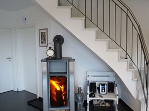 A room with a wood-burning stove, a clock, and a staircase.