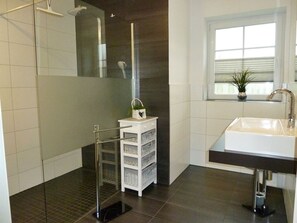 Une salle de bain moderne avec une douche à parois de verre, un meuble-lavabo blanc et une fenêtre avec des stores.