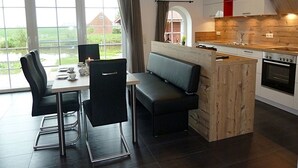 A modern kitchen with a dining area, large windows, and a view of the outdoors. - Riedhaus am Siel - 100sqm vacation home for 6 pers. + dog with fireplace, heat cabin & (Krummhörn)