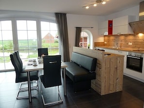 A modern kitchen with a dining area, large windows, and a view of the outdoors.