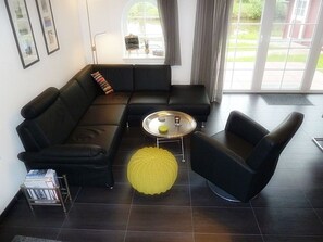 Una sala moderna con un sofá seccional negro, un pouf amarillo y una mesa de centro redonda.
