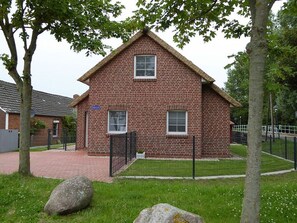 Une maison en briques avec deux fenêtres, un petit porche et une cour clôturée.