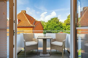 Ein Balkon mit Korbstühlen und einem Tisch, mit Blick auf ein Ziegelgebäude mit einem Ziegeldach.