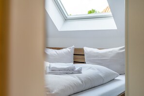 A bedroom with a skylight, white bedding, and a neatly made bed.