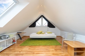 A small, triangular attic bedroom with a bed, a desk, and a chair. - Windrose - Beautiful, comfortable apartment in the best location of Greetsiel (Krummhörn)