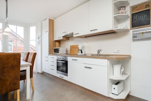 Een moderne keuken met witte kastjes, een inbouwoven, een magnetron en een koffiezetapparaat.