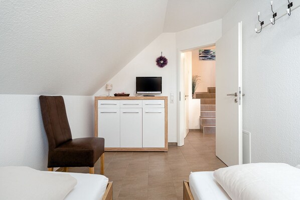 A modern bedroom with a bed, a chair, a TV on a cabinet, and a staircase leading to another room.