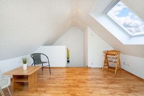 A spacious attic room with a sloped ceiling, a wooden floor, a dining table with chairs, a small plant, and a wooden ladder. - Windrose - Beautiful, comfortable apartment in the best location of Greetsiel (Krummhörn)