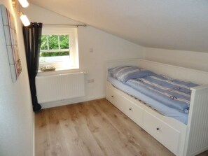 A small, single-bed room with a window, a radiator, and a wooden floor. - Gesine's Huuske - Gemütliches Ferienhaus im Eilsumer Ortskern (Krummhörn)