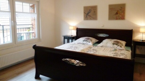 Une chambre à coucher avec un lit en bois, deux lampes fixées au mur, une fenêtre donnant sur un paysage agréable et deux tableaux encadrés accrochés au mur.