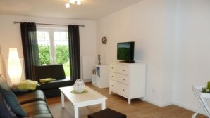 Un salon avec un canapé, une table basse, un téléviseur posé sur un meuble et une fenêtre avec des rideaux.