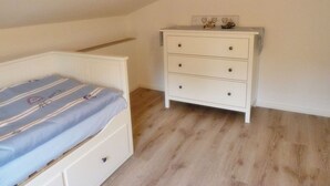A bedroom with a bed, a dresser, and a sloped ceiling. - Gesine's Huuske - Gemütliches Ferienhaus im Eilsumer Ortskern (Krummhörn)