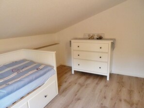 A bedroom with a bed, a dresser, and a sloped ceiling. - Gesine's Huuske - Gemütliches Ferienhaus im Eilsumer Ortskern (Krummhörn)