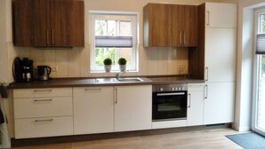 Une cuisine moderne avec des meubles blancs, un four encastré et une fenêtre donnant sur un paysage verdoyant.
