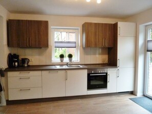 A modern kitchen with white cabinets, a built-in oven, and a window with a view of greenery.