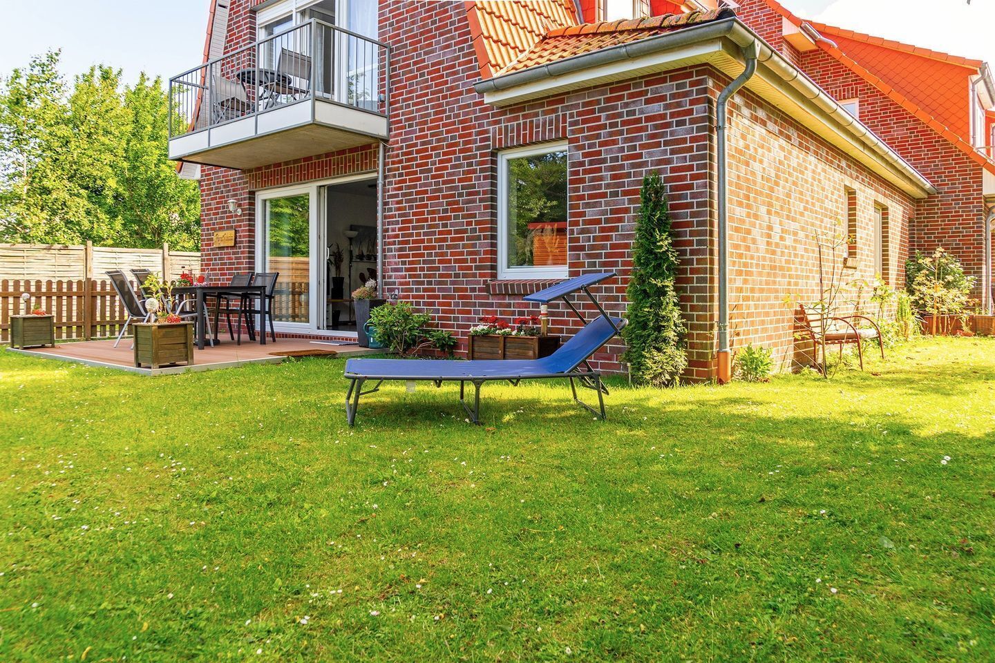 A red brick house with a balcony, a patio with outdoor furniture, and a grassy yard.