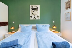 Una cama doble con dos almohadas y dos lámparas de noche, una pared verde y un cuadro enmarcado sobre la cama.