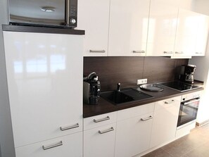 A modern kitchen with white cabinets, a dark countertop, a coffee maker, and an oven.