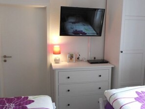 Una camera da letto con una TV montata a parete, un comodino con una lampada e un letto con biancheria da letto a motivi floreali.