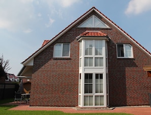 A two-story house with a red brick exterior, a central bay window, and a sloped roof.