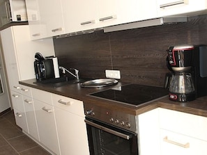 Una cucina moderna con mobili bianchi, un piano di lavoro in legno scuro, un piano cottura integrato e una macchina per il caffè.