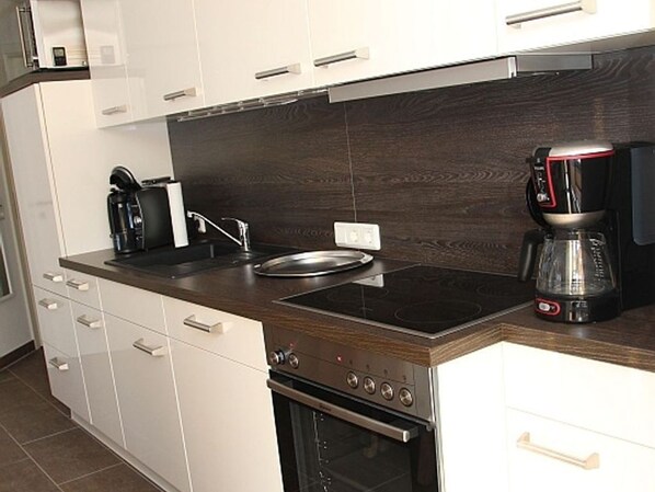 A modern kitchen with white cabinets, a dark wood countertop, a built-in stove, and a coffee maker.