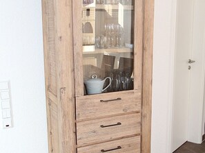 A wooden cabinet with a glass door containing kitchenware.