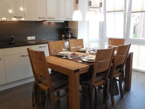 A modern kitchen with white cabinets, a wooden dining table set for six, and a large window providing natural light.