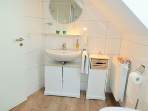 Ein modernes Badezimmer mit Waschbecken, Spiegel und Schränken in Weiß. Ein Handtuch hängt an der Schranktür.