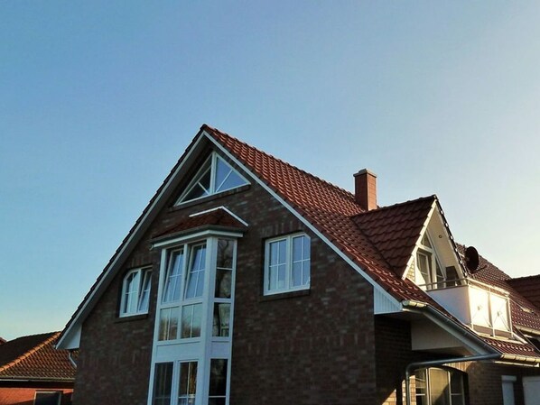Ein zweistöckiges Haus mit rotem Ziegeldach, einem markanten Erker im ersten Obergeschoss und einem Schornstein.