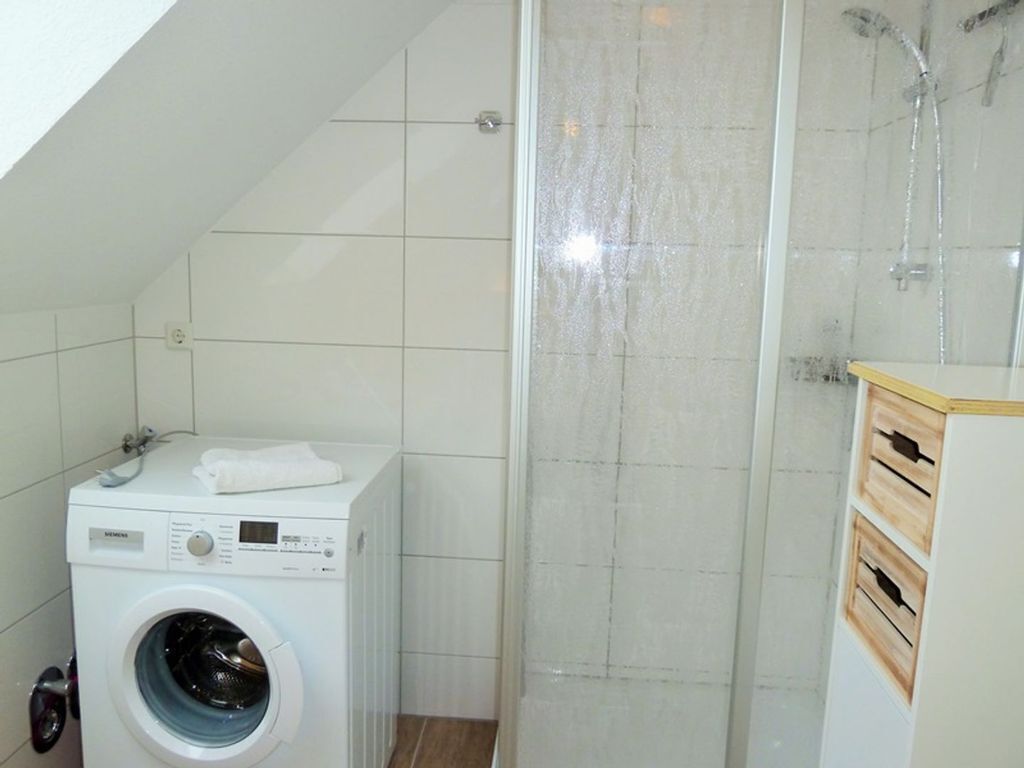 Un baño pequeño con lavadora, cabina de ducha y un armario de madera.